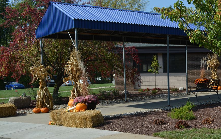 An outdoor area decorated with pumpkins, hay bales, and corn stalks beneath a blue canopy.