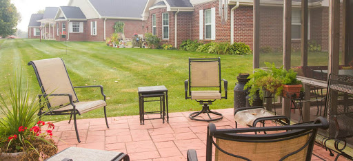 A cozy outdoor patio set up with chairs and a small table, surrounded by lush green grass and a brick home.