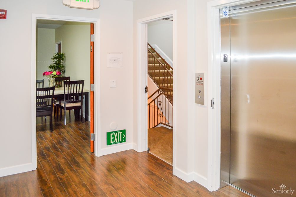 A hallway with an elevator and a staircase, featuring wooden flooring and an exit sign.