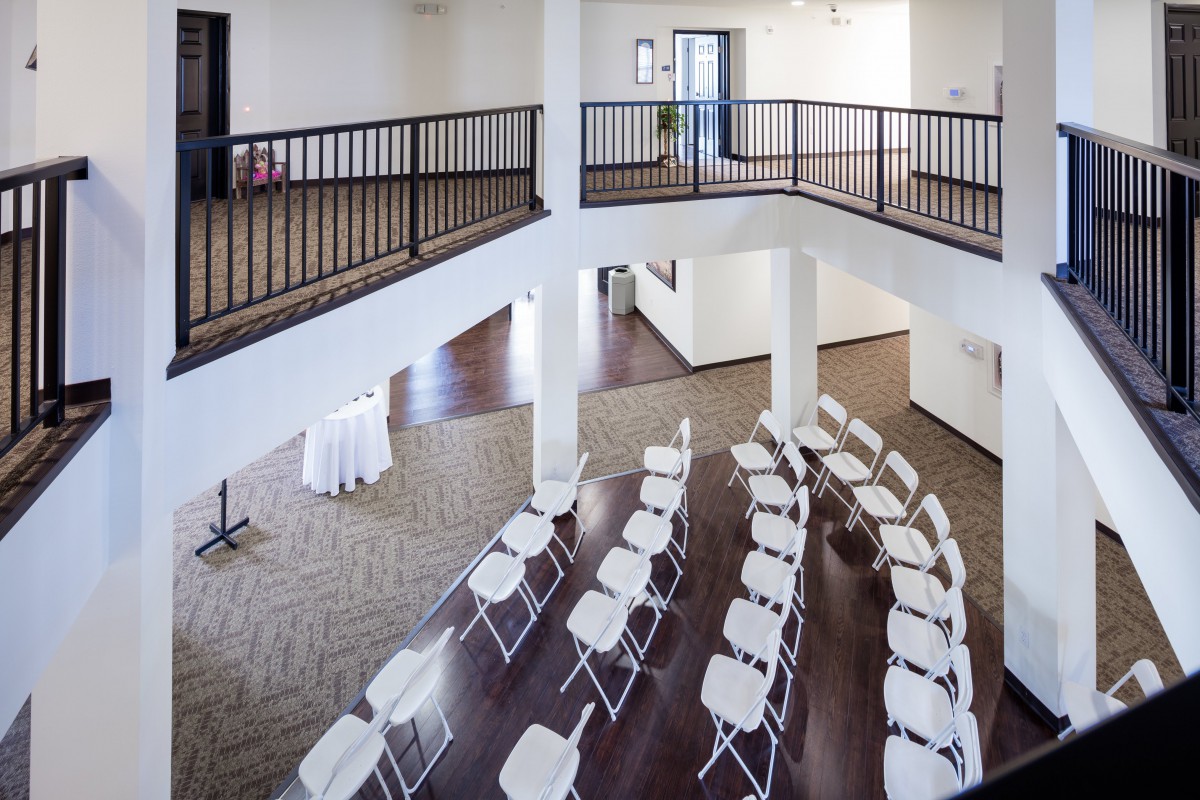 A modern indoor event space with rows of chairs arranged for a conference or meeting, featuring a balcony overlooking the area.