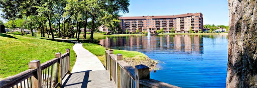 A serene view of a lake surrounded by lush greenery and a residential building reflecting on the water's surface.