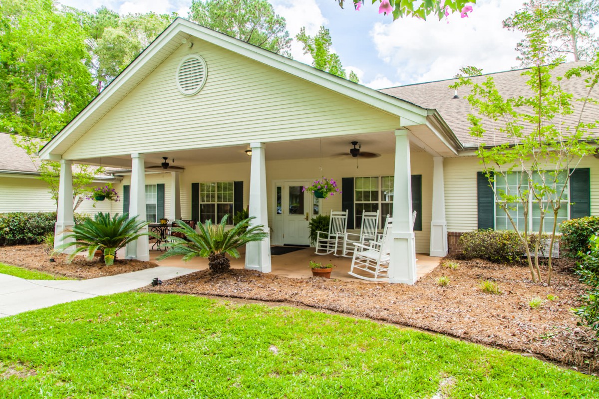 A charming house with a welcoming front porch, featuring rocking chairs and surrounded by well-maintained landscaping.
