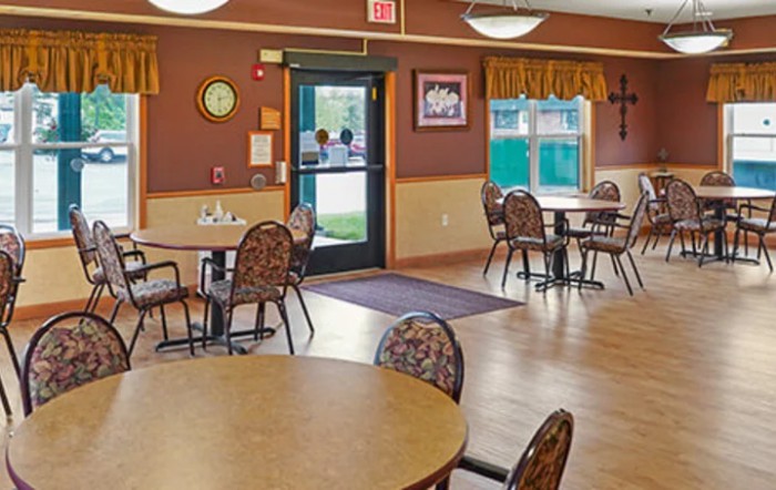 An empty dining room with tables and chairs arranged on a wooden floor.