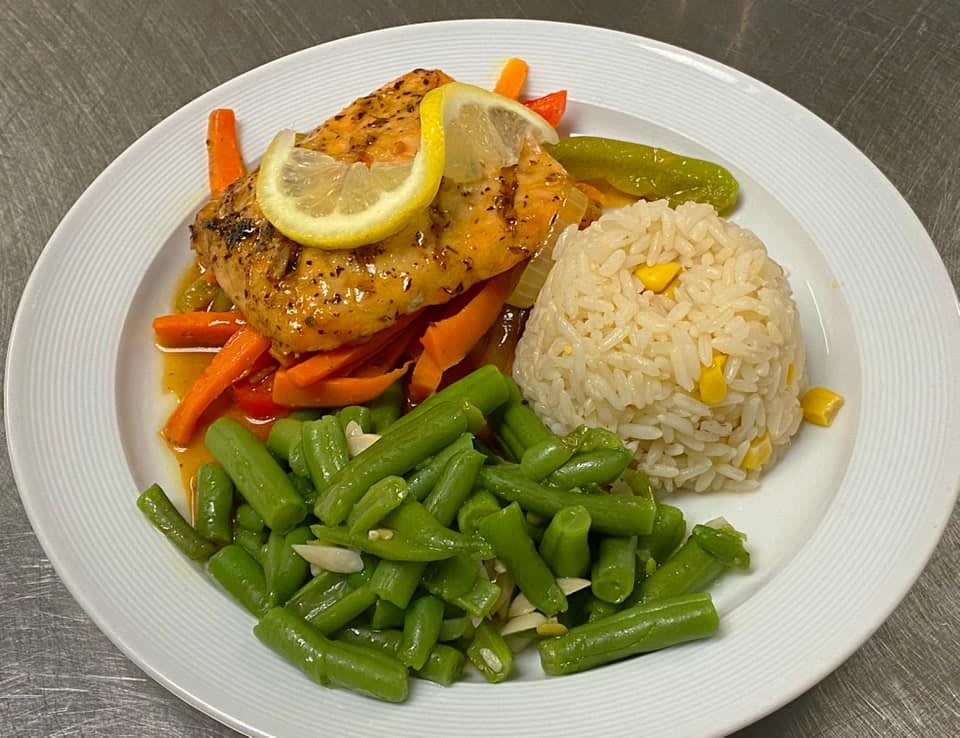 A plate of grilled salmon with mixed vegetables, rice, and a lemon slice.