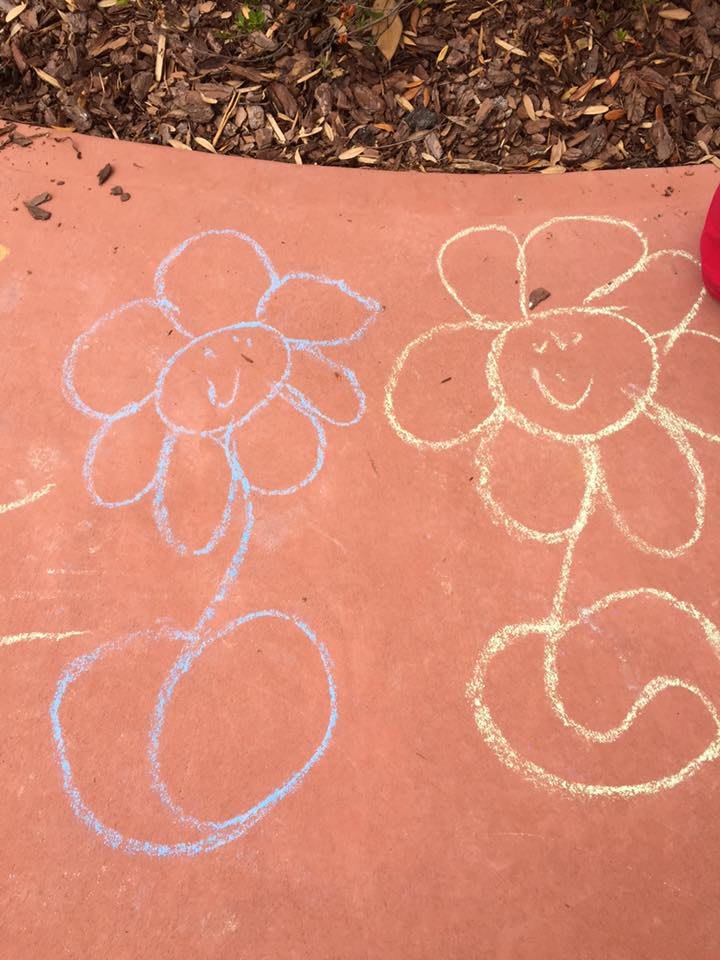 Chalk drawings of smiling flowers on a sidewalk.