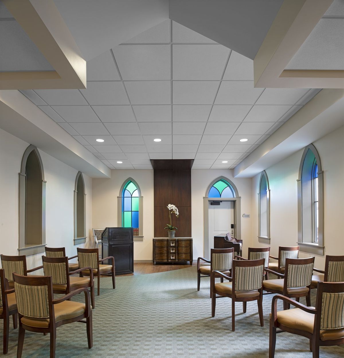 A small chapel interior with seating arrangements and arched windows.