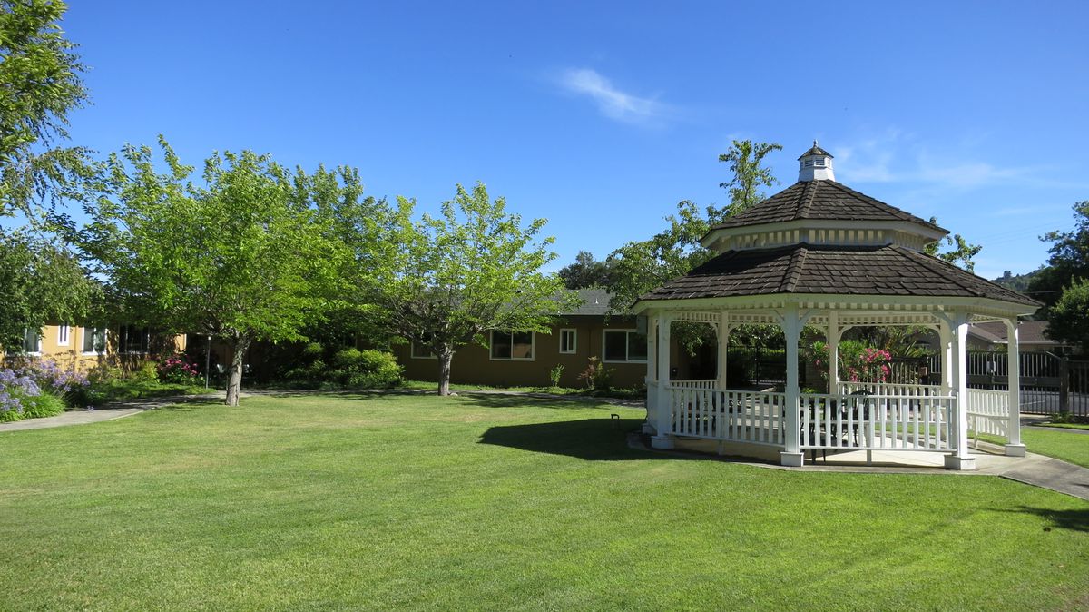 A serene outdoor setting with a gazebo, lush lawn, and trees under a clear blue sky.