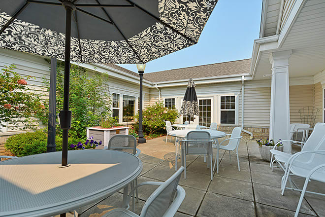 A cozy backyard patio with tables, chairs, and umbrellas surrounded by greenery.
