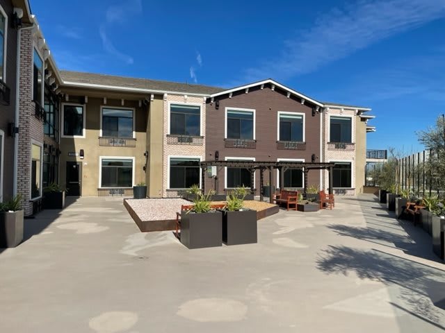 A modern two-story building with large windows and an outdoor patio area under a clear blue sky.
