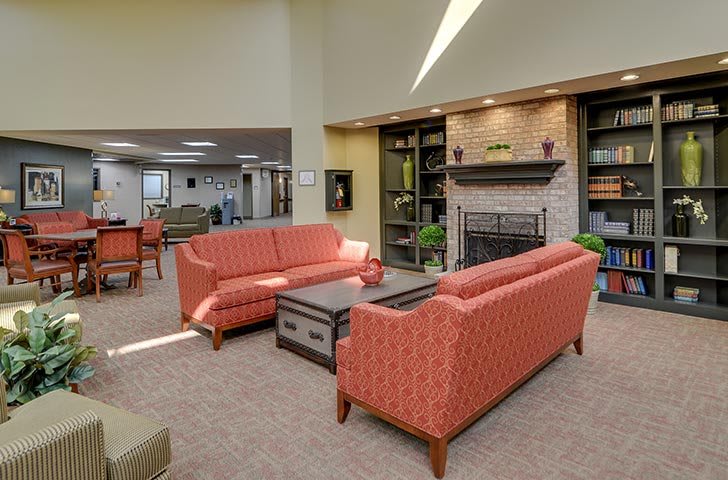 A cozy living room with red couches, a central coffee table, and a brick fireplace surrounded by shelves.