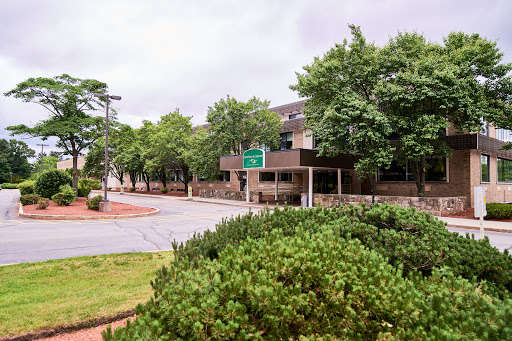 A view of a building surrounded by green trees and shrubbery, with a road sign visible in the foreground.