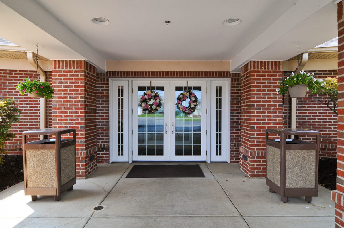 The image shows the entrance of a brick building with double glass doors adorned with decorative wreaths. Trash cans are placed on either side.