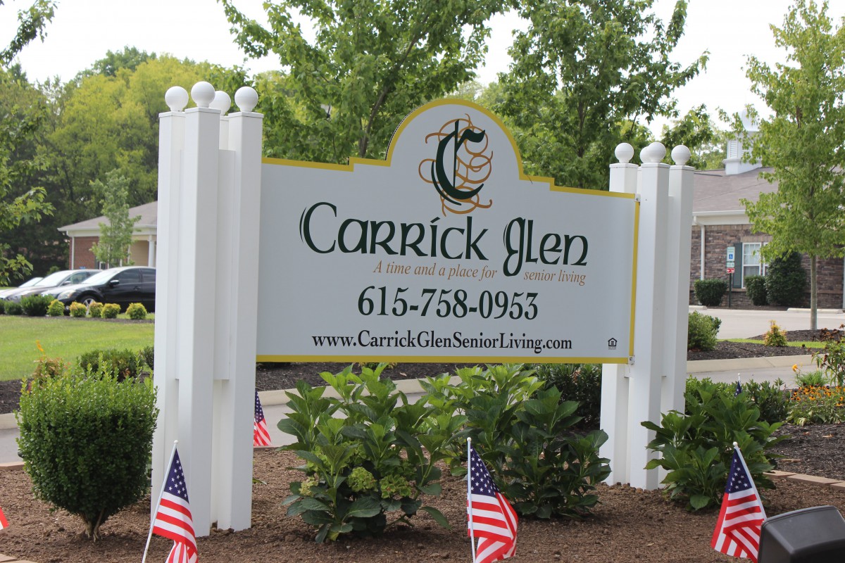 Entrance sign for Carrick Glen with contact information and American flags.