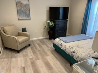 A cozy bedroom featuring a bed with floral bedding, a TV on a dresser, and a comfortable chair.