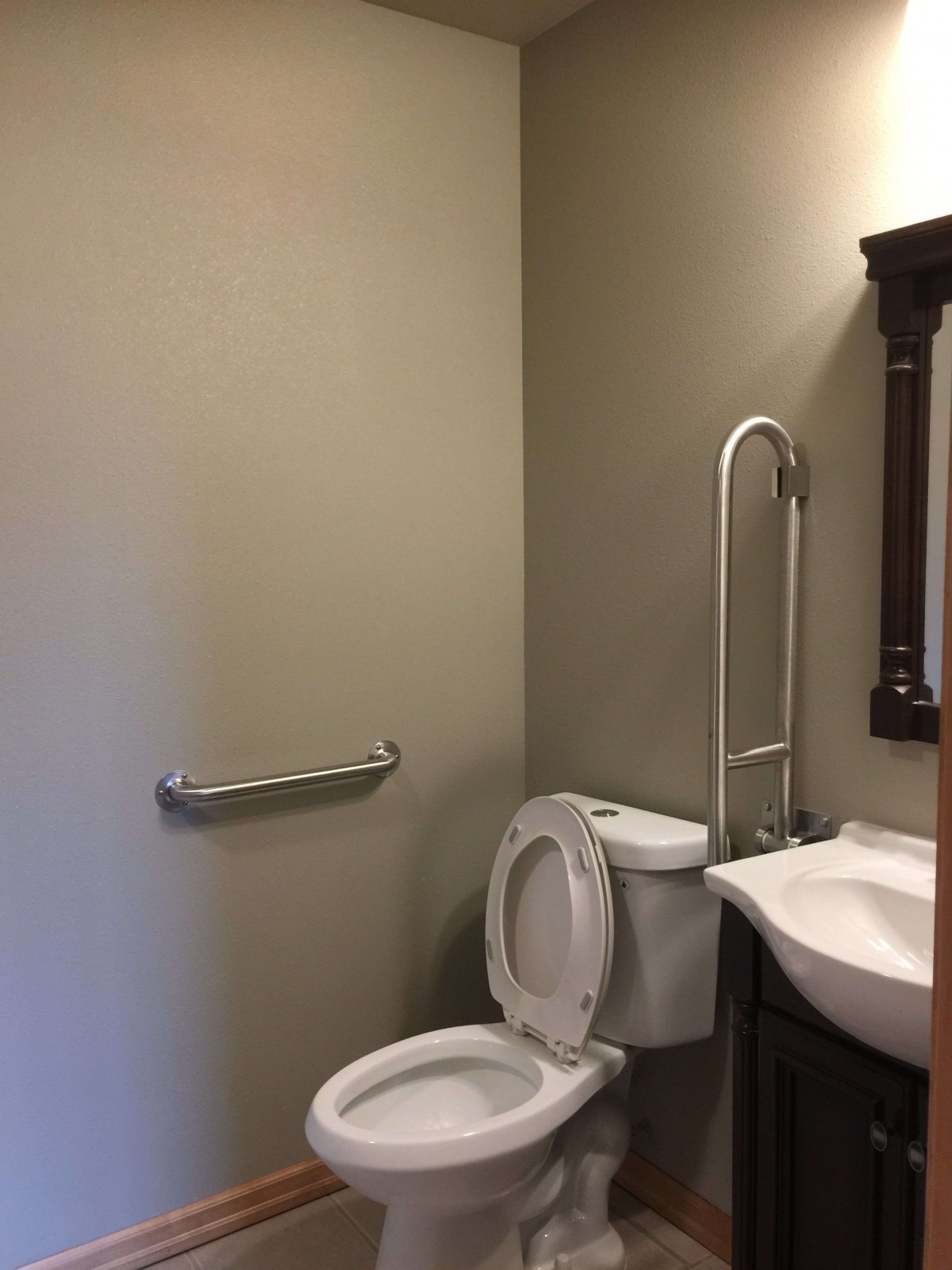 A small bathroom with a toilet, sink, mirror, and handrail.
