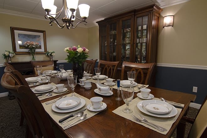 A formal dining room with an elegantly set table, featuring fine dinnerware and a floral centerpiece.