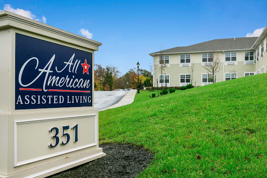 Entrance sign of All American Assisted Living with a view of the facility and surrounding greenery.