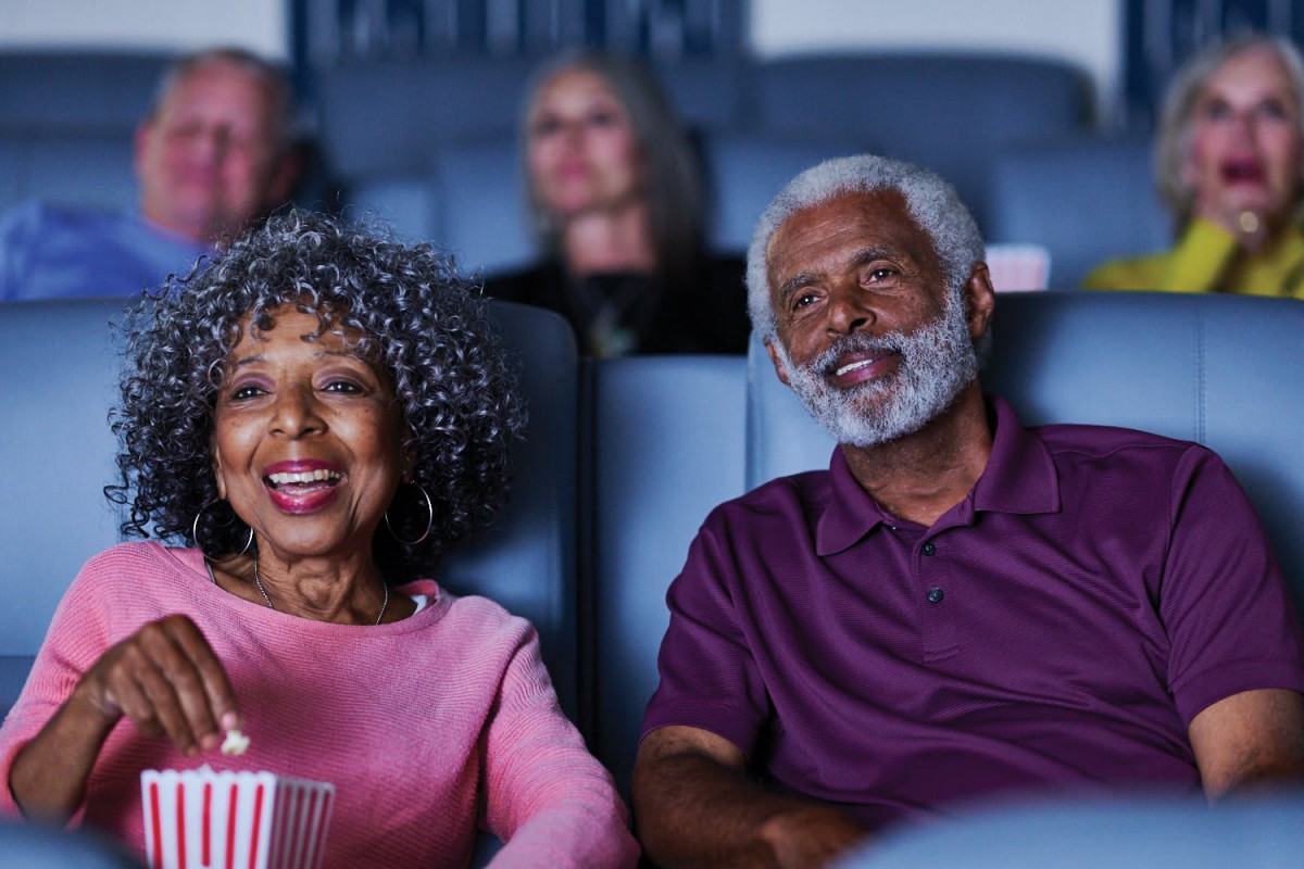 An elderly couple enjoying a movie together in the cinema, sharing popcorn and smiles.