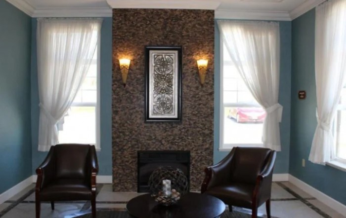 A cozy living room with a stone fireplace, elegant chairs, and soft curtains framing the windows.