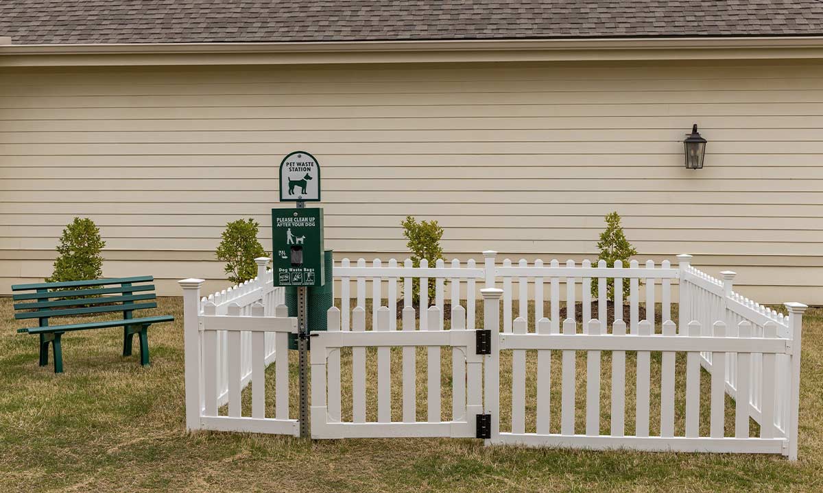 A white picket fence encloses a small yard with a dog waste disposal sign, adjacent to a house.