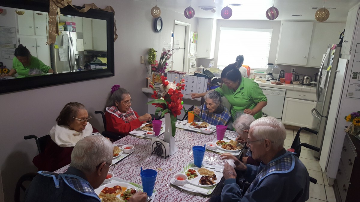 A group of elderly people sharing a meal together with caregivers in a cozy dining setting.