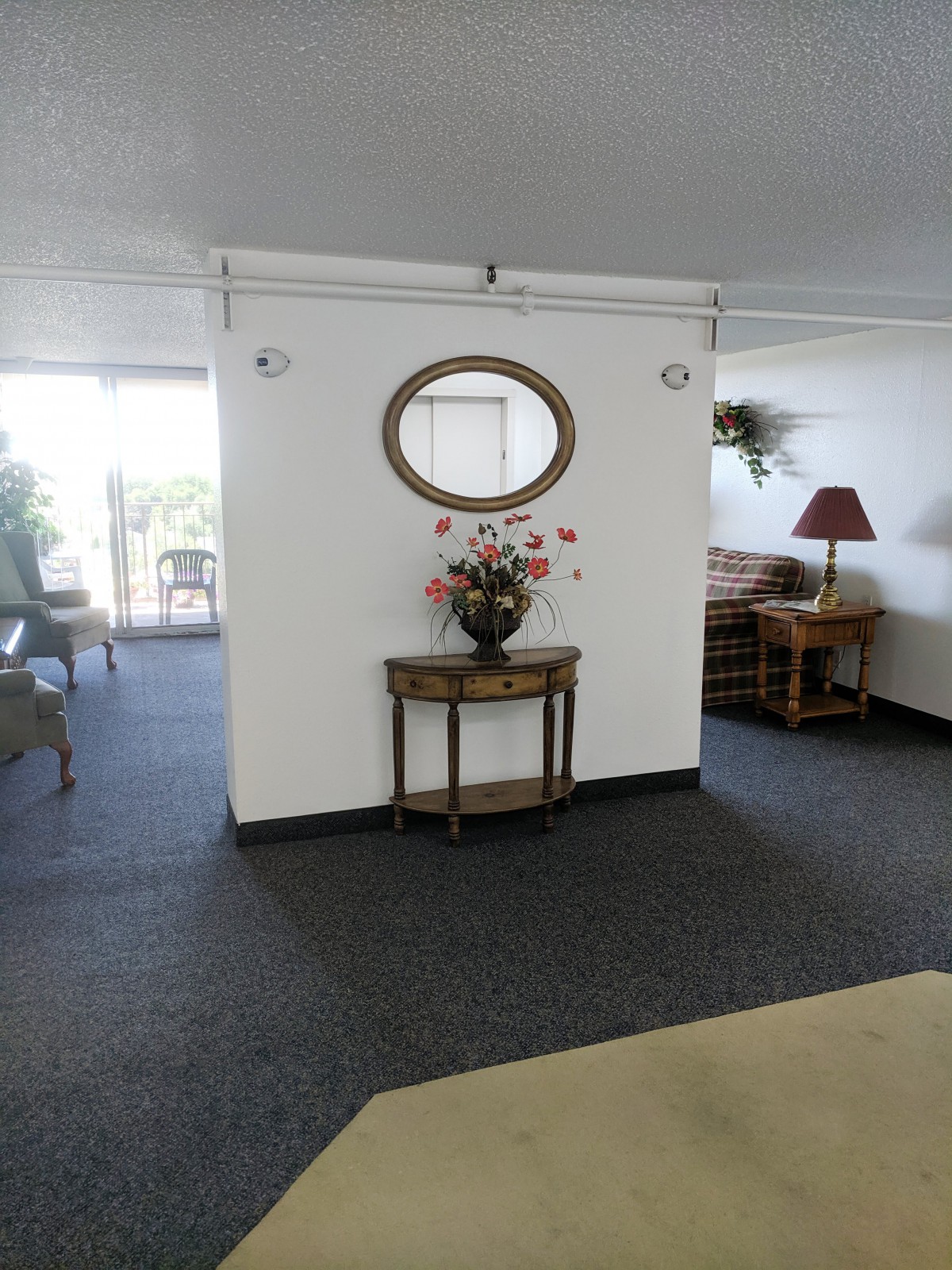 A cozy living room interior featuring a wall-mounted mirror and a decorative table with flowers.