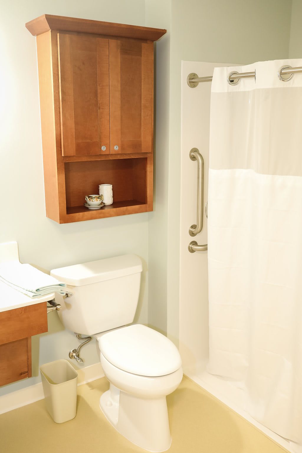 A clean and well-organized bathroom featuring a toilet, shower with a white curtain, and a wooden storage cabinet.
