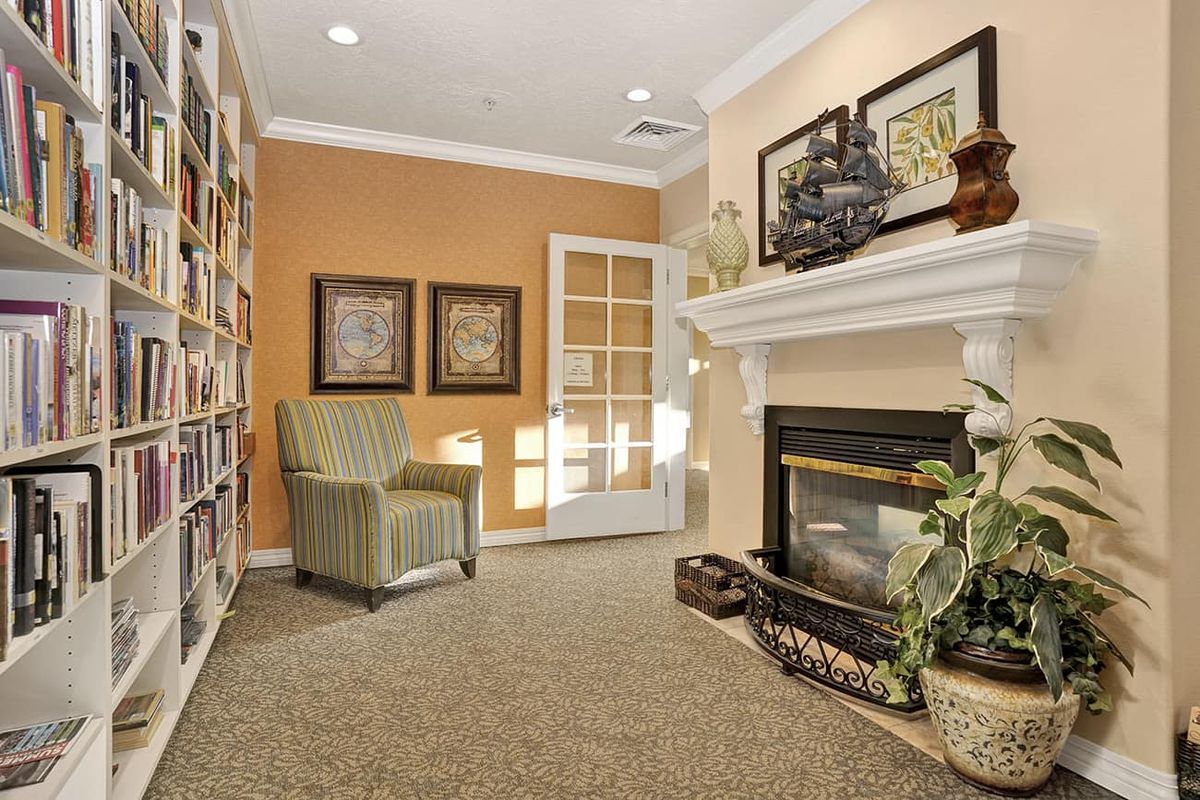 A cozy living room with a fireplace, an armchair, and a bookshelf filled with books.