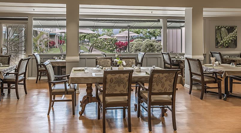 A well-appointed dining room with elegantly set tables and chairs, providing a pleasant window view of the outdoors.