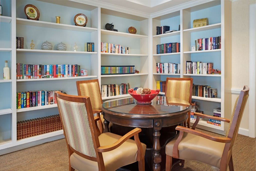 A cozy library corner with bookshelves and a round table surrounded by armchairs.