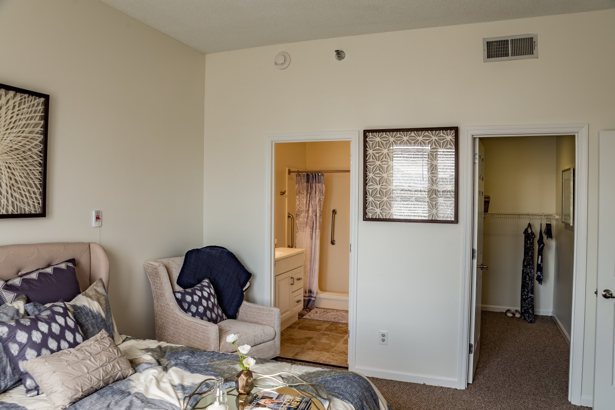 A cozy bedroom with a chair, decorative items, and an open doorway leading to a bathroom.