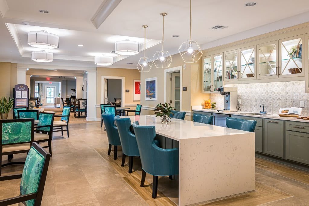 A modern kitchen and dining area featuring a large table with teal chairs and pendant lighting.