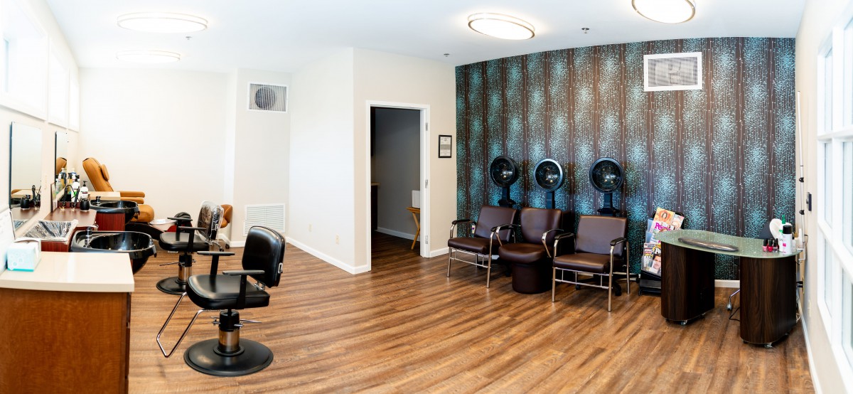 A modern hair salon interior featuring wood flooring, styling chairs, and hooded hair dryers.