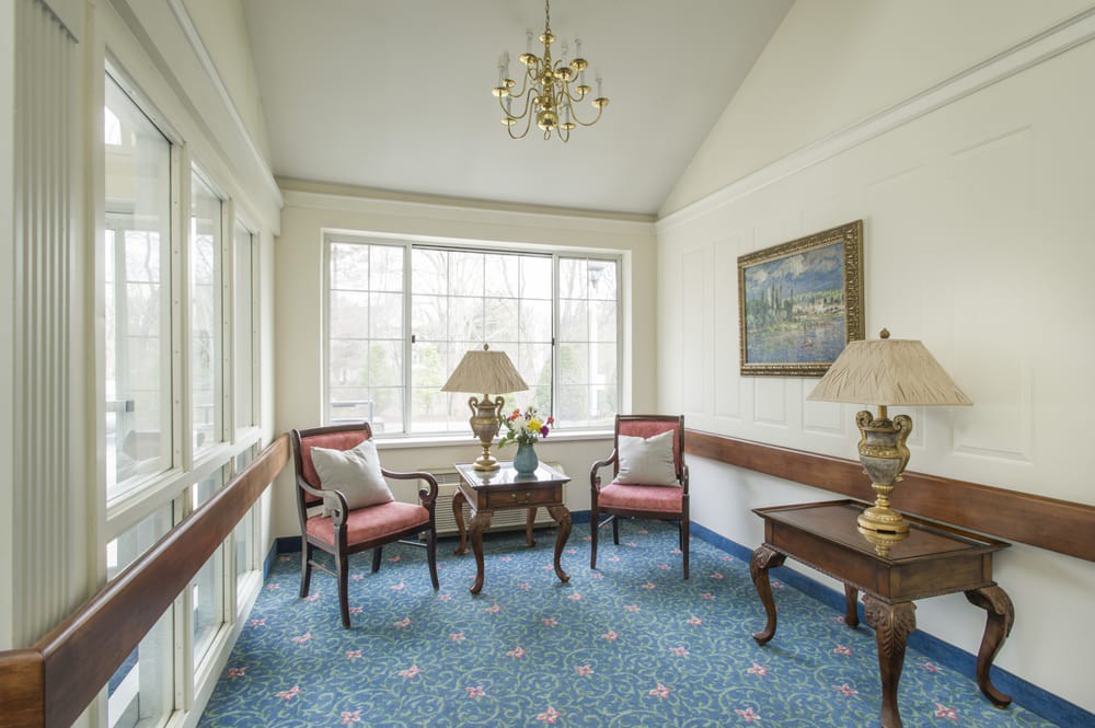 A cozy sitting area featuring two chairs, a small table with lamps, and a large window letting in natural light.