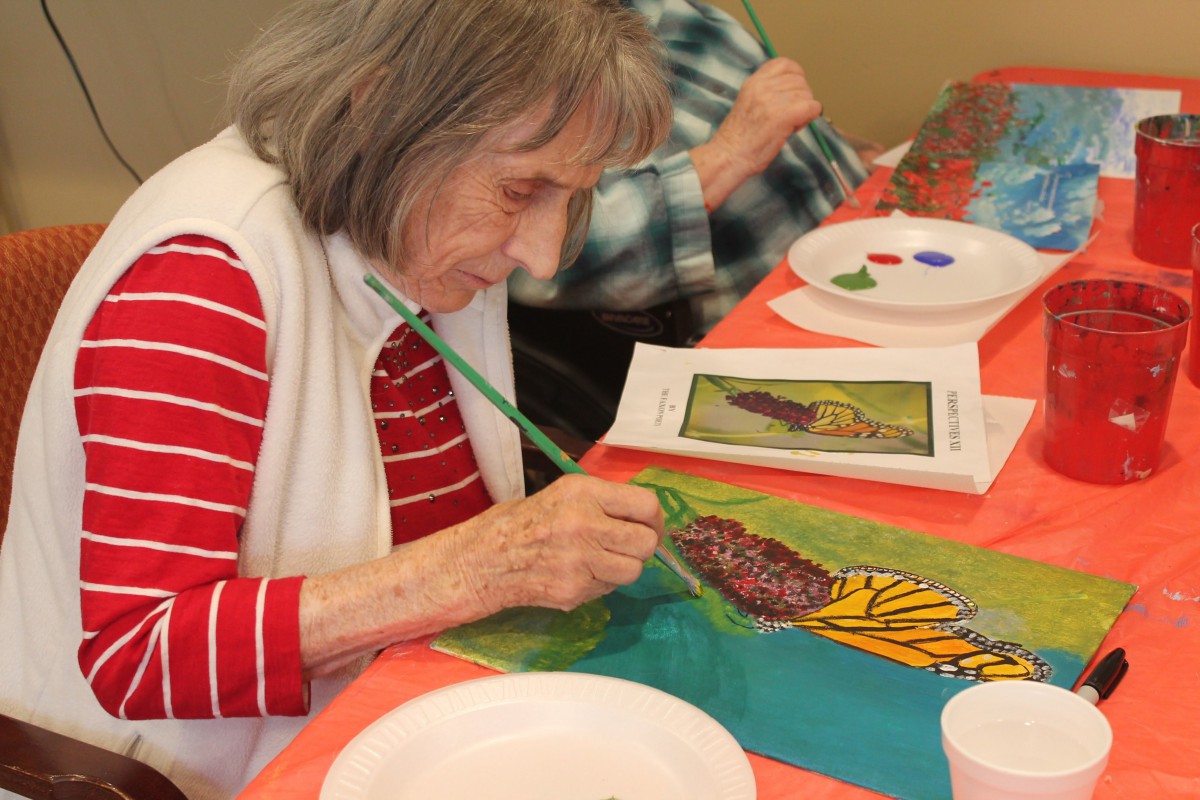 An elderly woman painting a colorful artwork at a table.