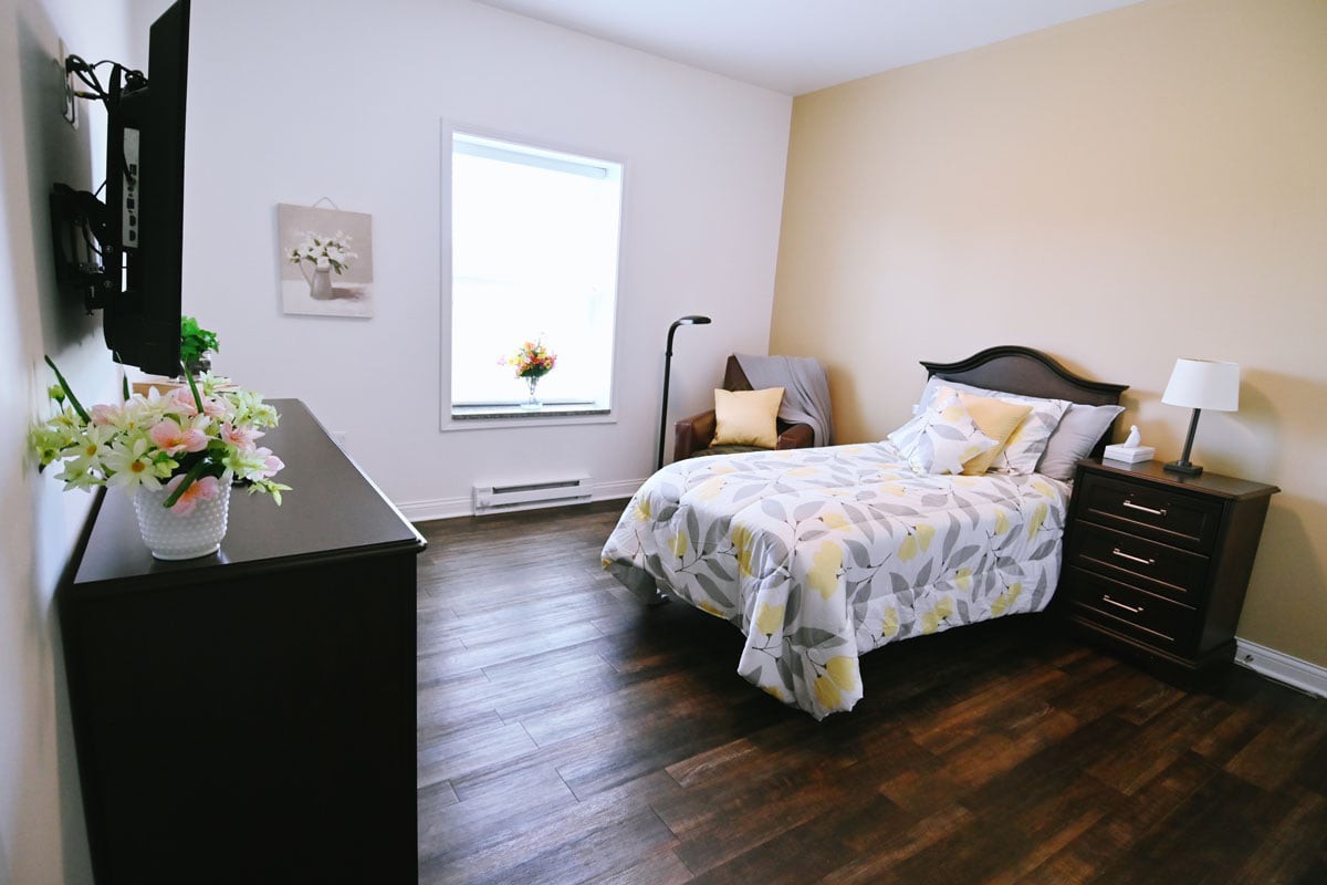A cozy bedroom with a bed, chair, lamp, and wooden flooring.