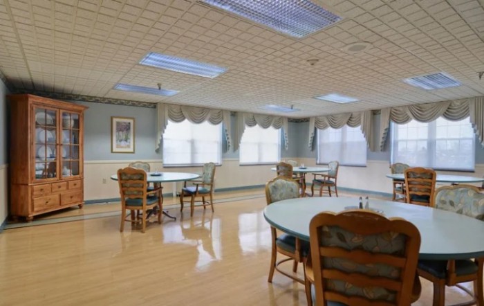 A quiet dining area with several tables and chairs, featuring large windows with curtains.