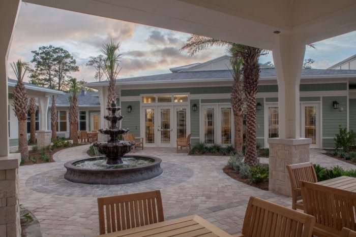 A tranquil courtyard with a central fountain, surrounded by palm trees and outdoor seating.