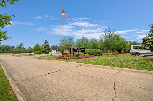 A scenic view of a park entrance featuring a flag and well-maintained greenery under a clear blue sky.