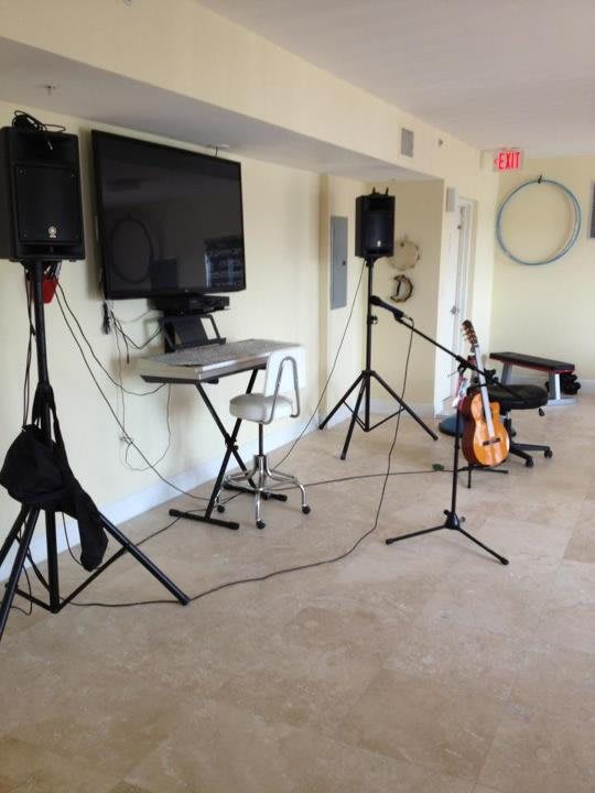 An indoor music setup featuring speakers, a guitar, microphone stands, and a television.