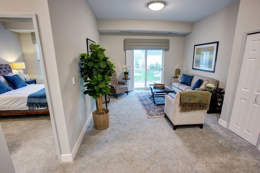 A cozy living room with a sofa, armchair, artwork on the walls, and a large window allowing natural light.