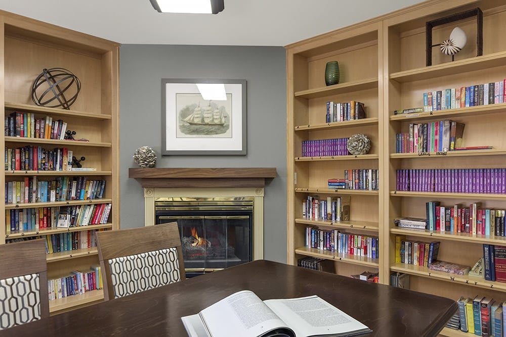 A cozy library room with wooden bookshelves, a fireplace, and an open book on the table.