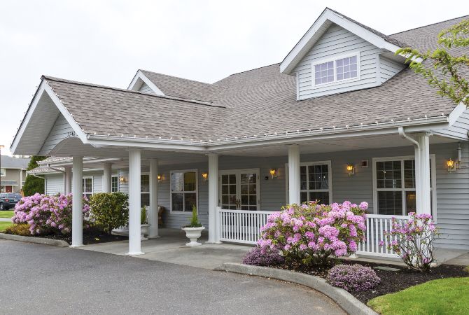 A residential building with a porch and blooming flowers in the front yard.