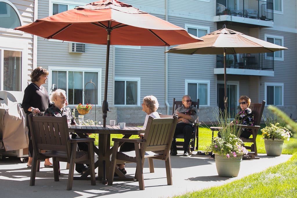 People sitting and conversing on a sunny patio with umbrellas.