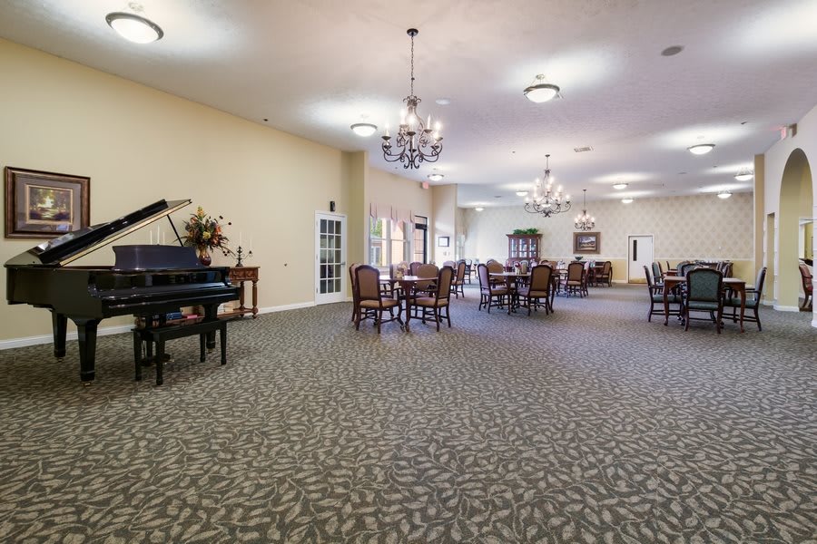 A spacious dining room with a grand piano and elegant chandeliers.