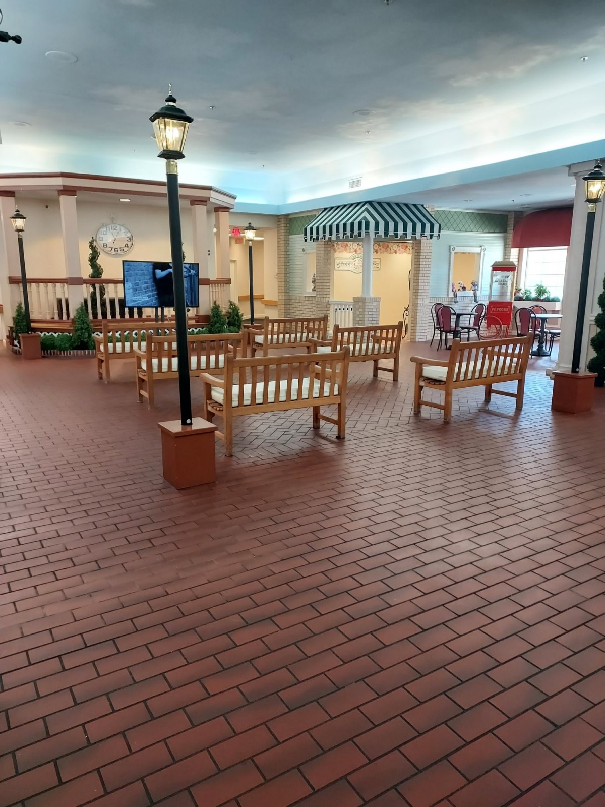 An indoor shopping area featuring benches, brick flooring, and shop fronts with decorative elements.