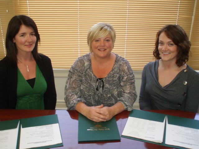 Three women sitting at a table with documents in an office setting.