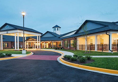 A well-lit building entrance with a landscaped driveway during the evening.