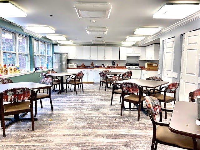 A modern dining area with several tables and chairs, featuring a kitchen in the background.