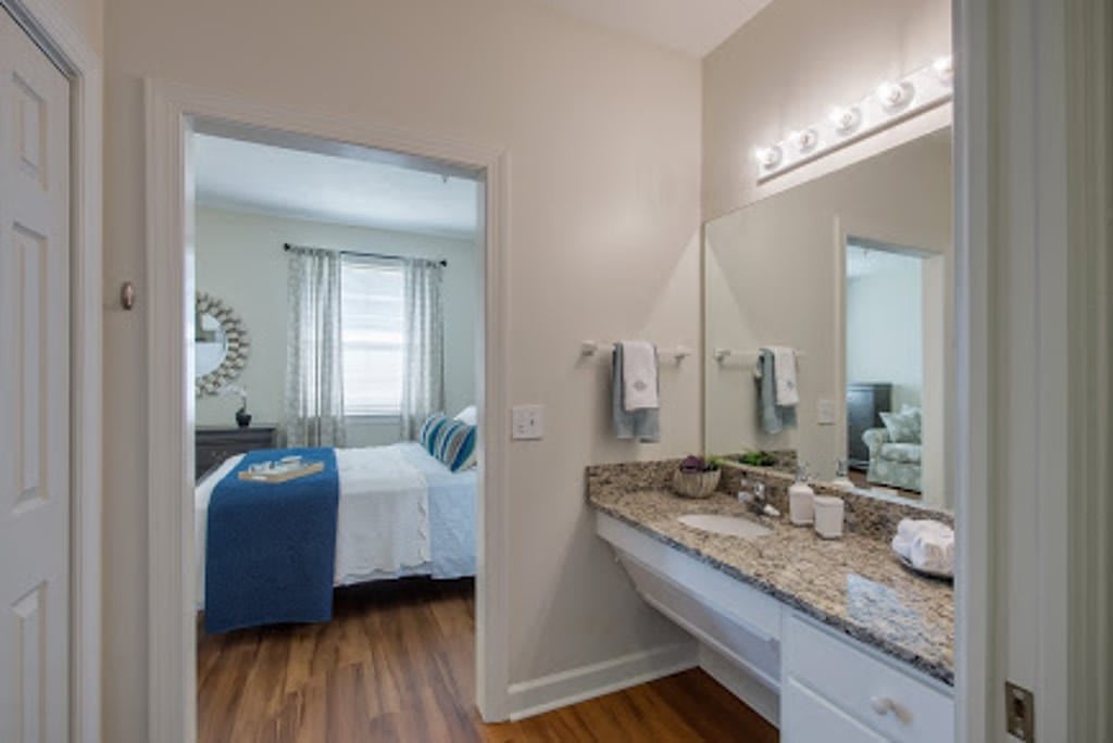 A modern bathroom with a granite countertop and wood flooring, connected to a cozy bedroom.